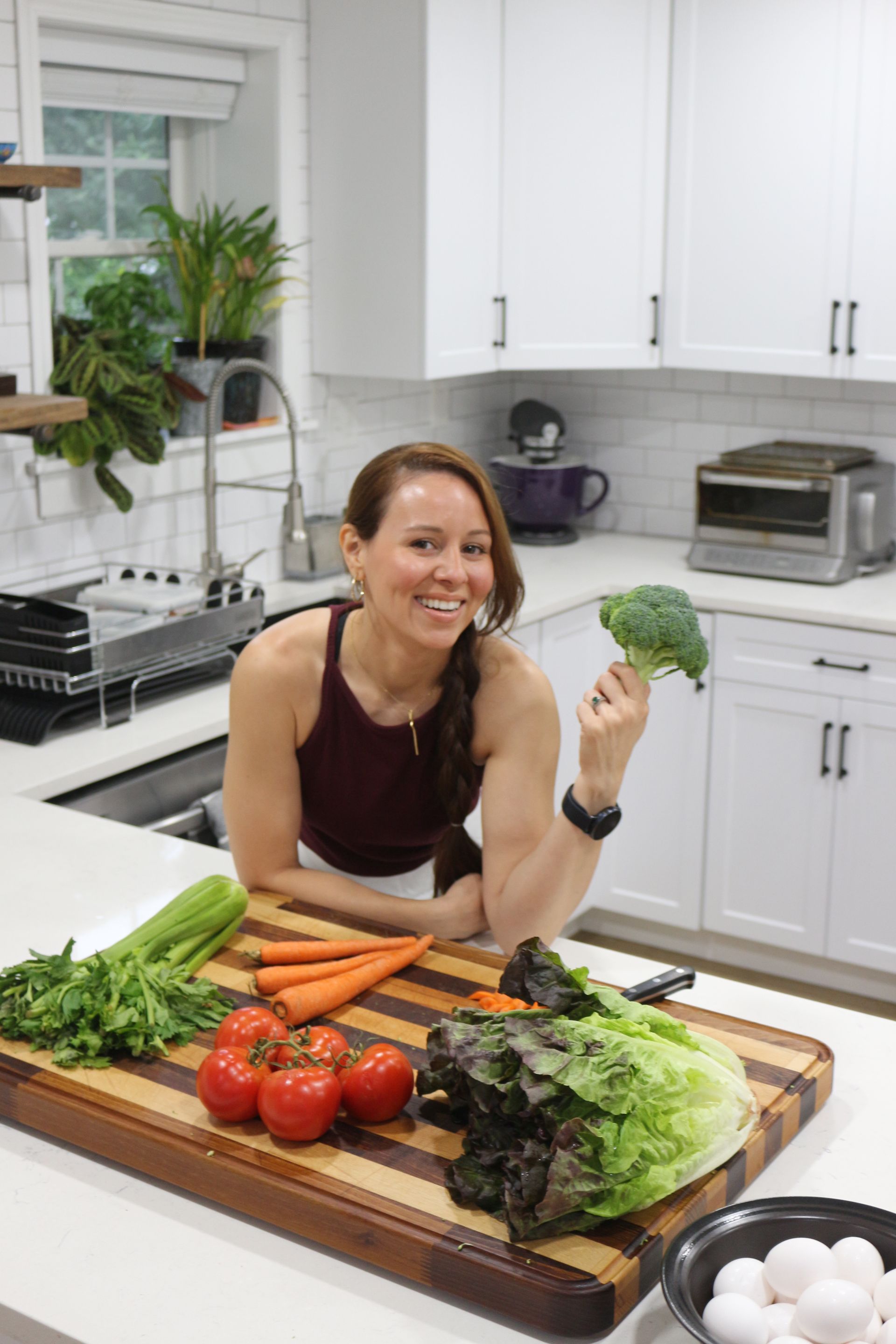 A woman is sitting at a kitchen counter holding a broccoli.