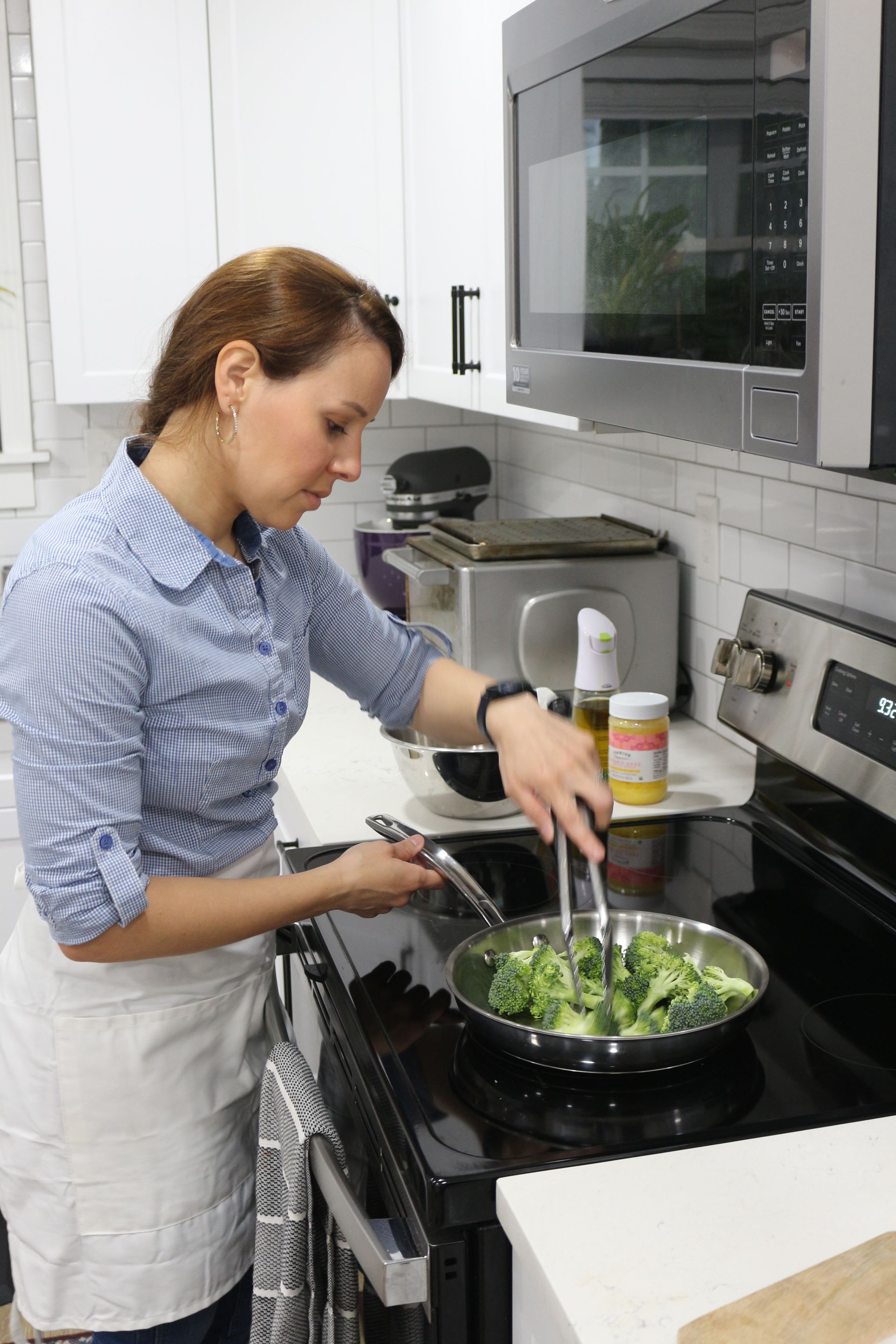 A woman is cooking vegetables on a stove in a kitchen.