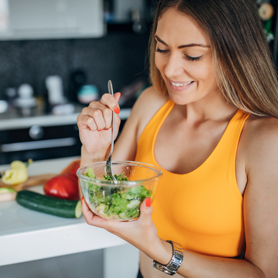 A woman is eating a salad from a bowl with a spoon.