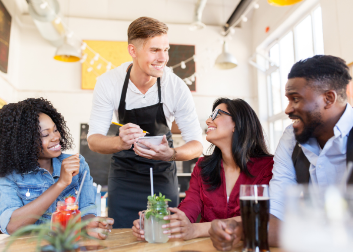 A group of people are sitting at a table in a restaurant while a waiter serves them food.