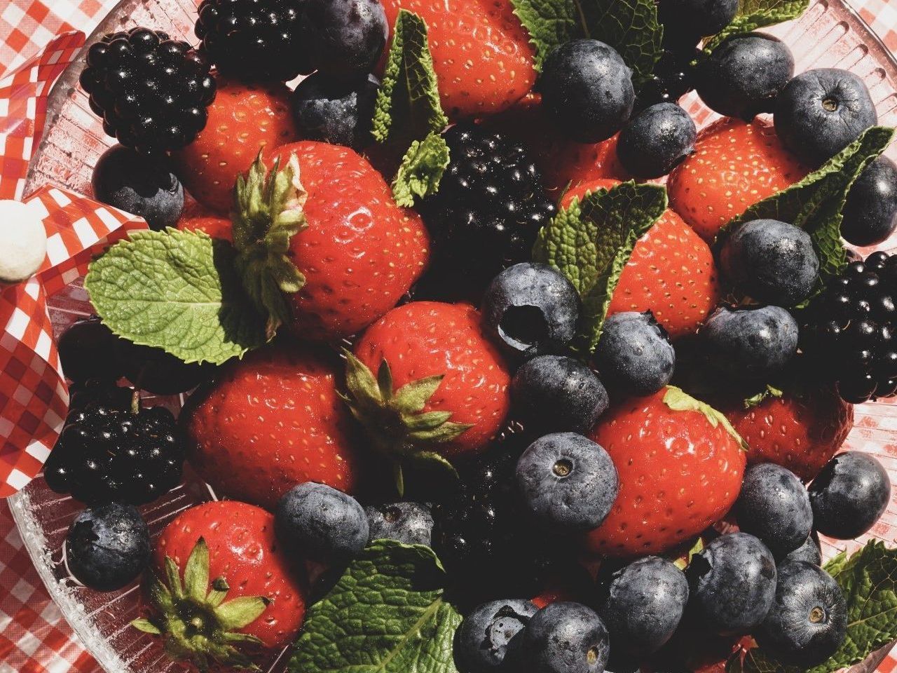 A glass bowl filled with strawberries , blueberries , blackberries and mint leaves.