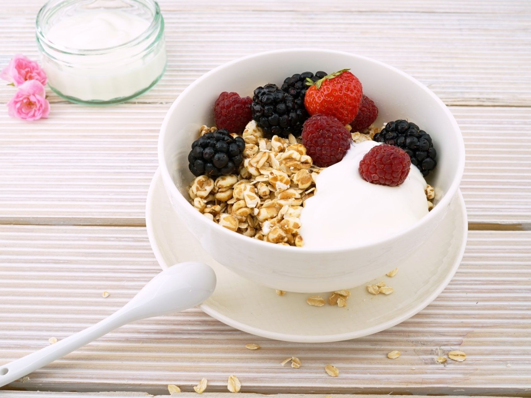 A bowl of granola with yogurt and berries on a wooden table.