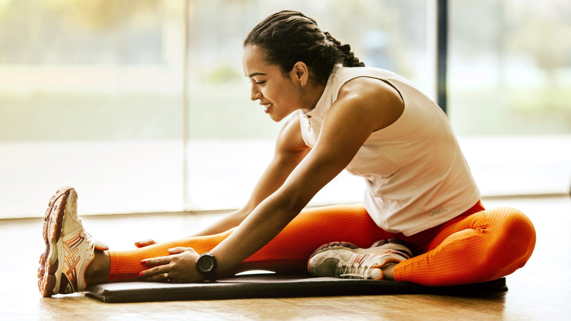 A woman is sitting on the floor stretching her legs.