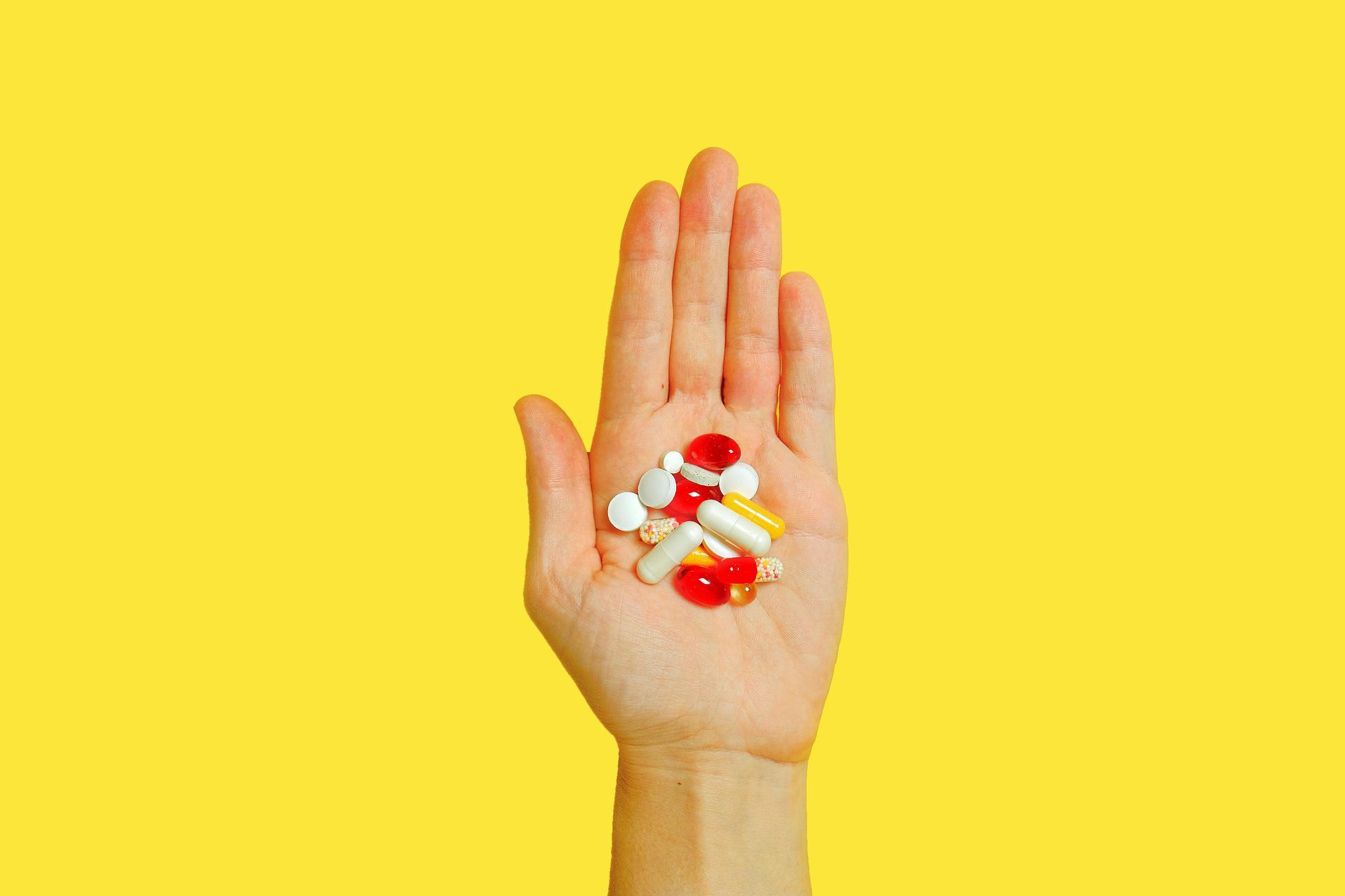 A hand is holding a pile of pills on a yellow background.