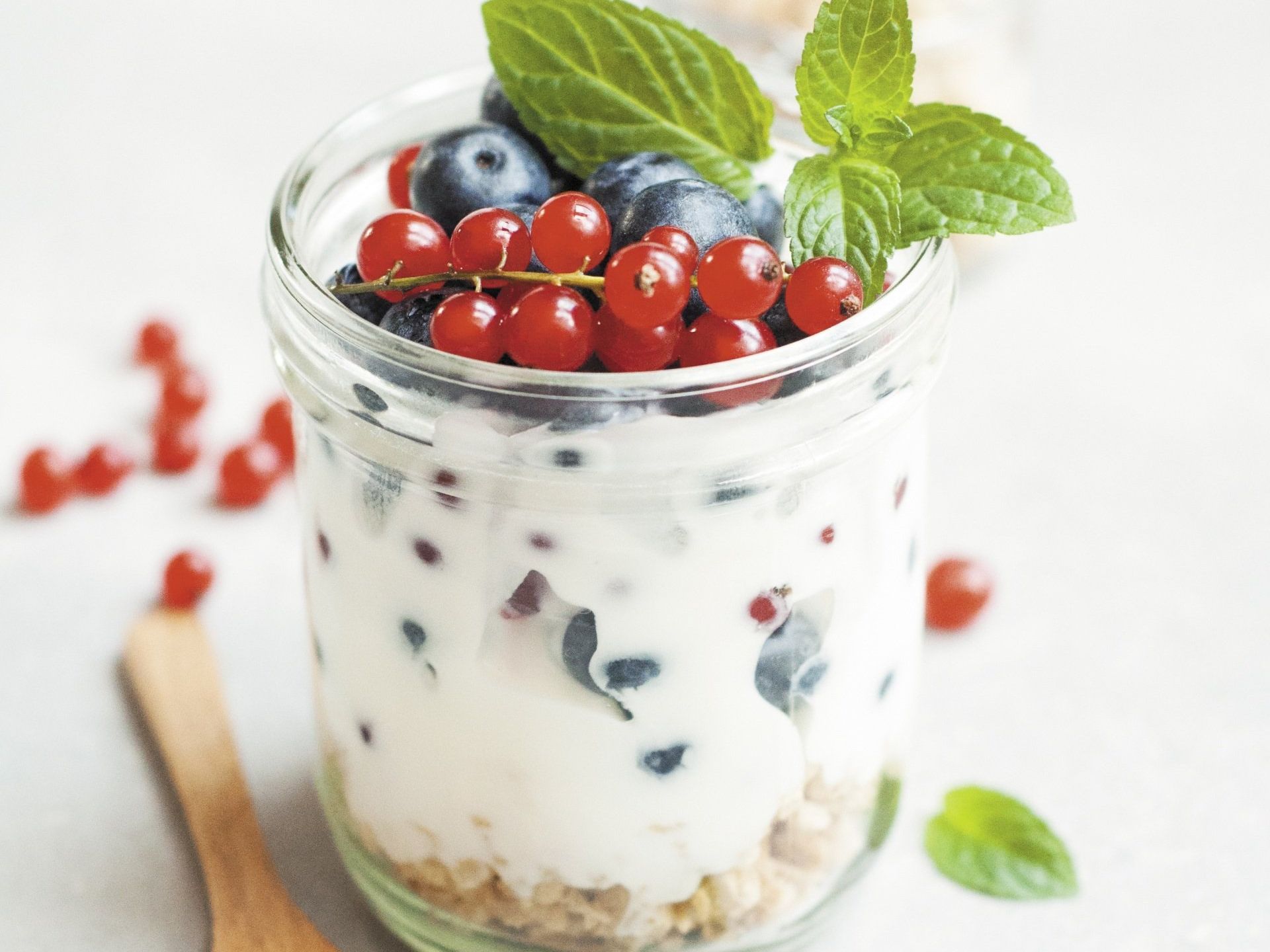 A jar of yogurt with blueberries and red currants on top.