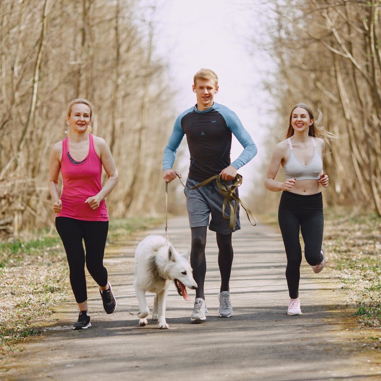 A man and two women are running with a dog on a leash