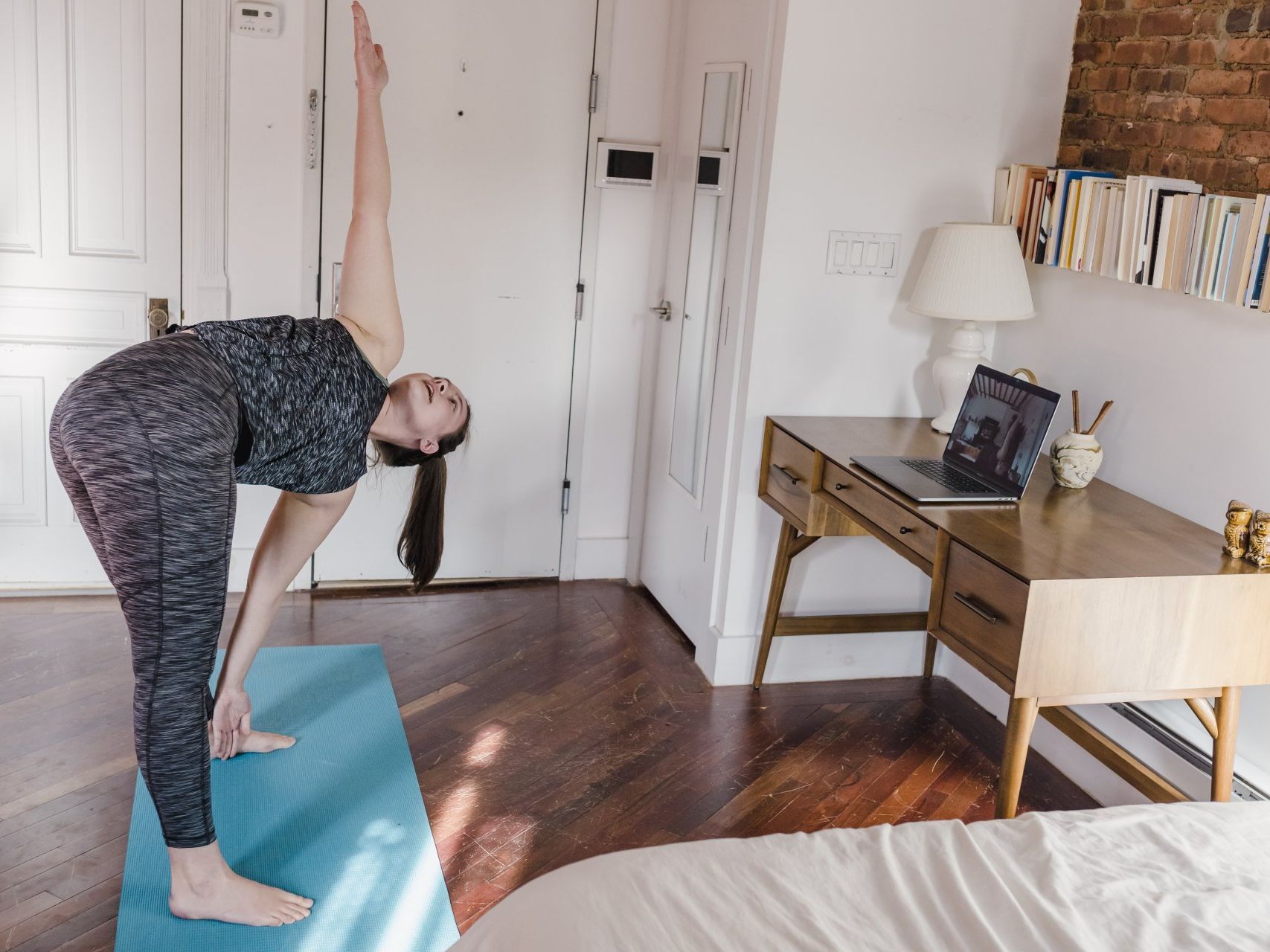 A woman is doing a yoga pose on a yoga mat in a bedroom.