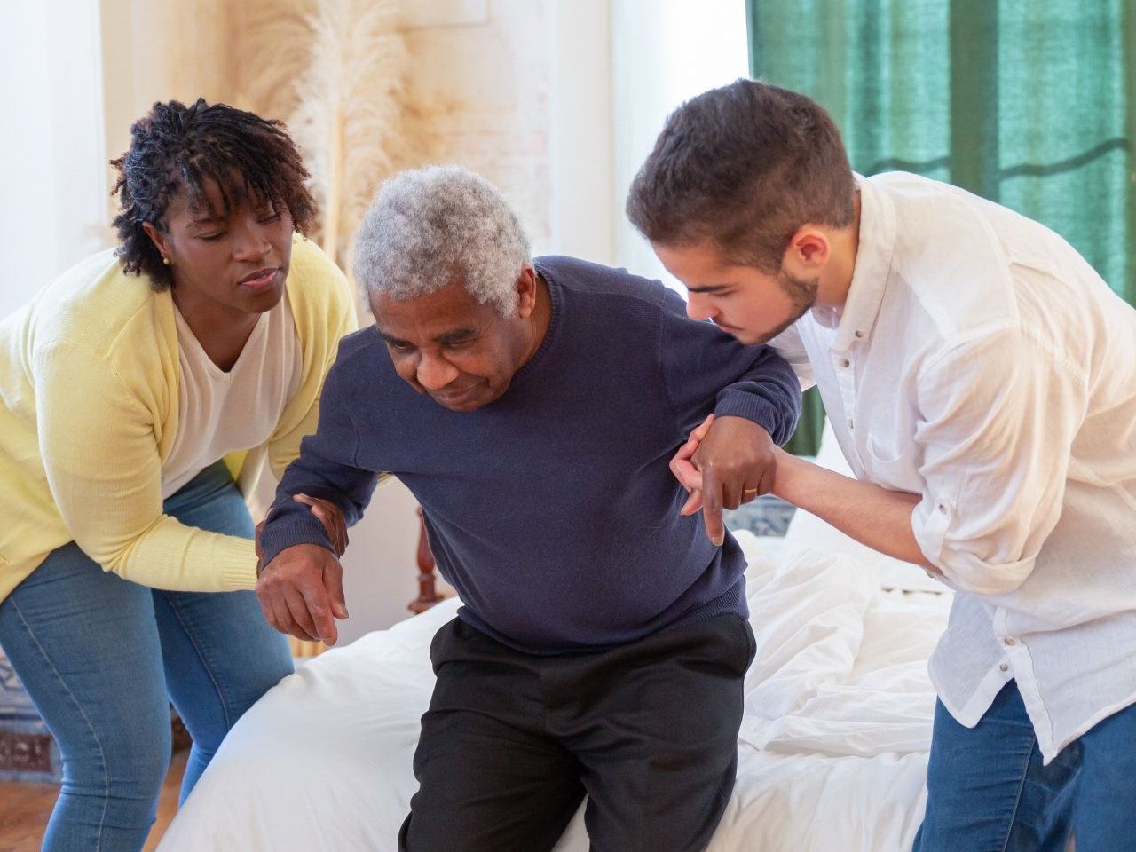 A group of people are helping an elderly man get out of bed.