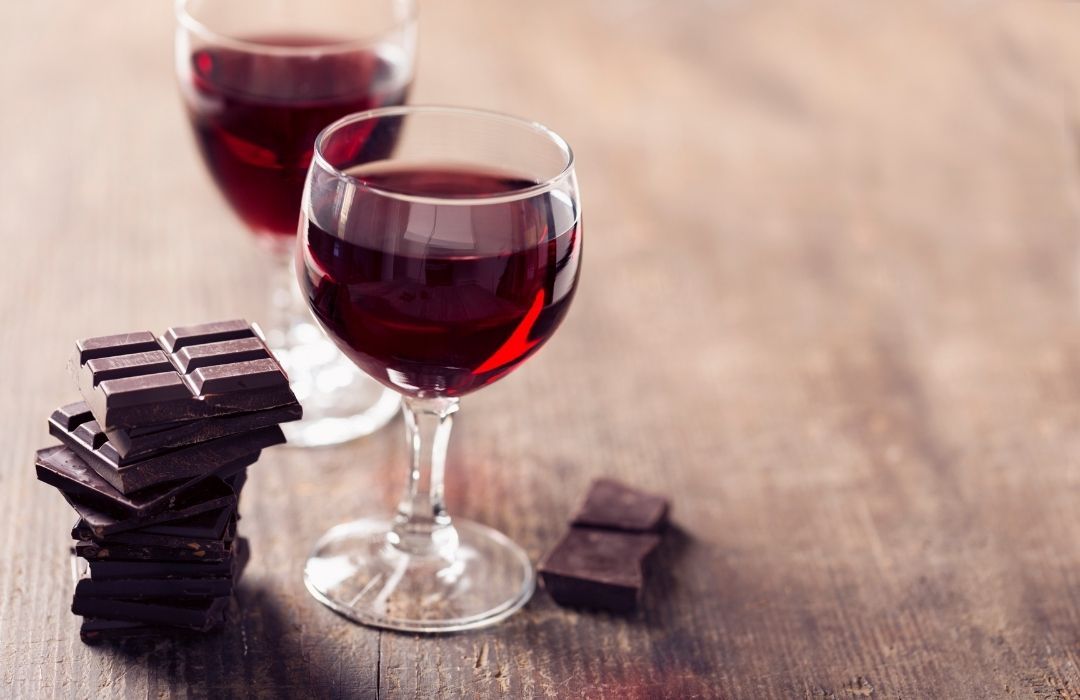 Two glasses of red wine and a stack of chocolate bars on a wooden table.