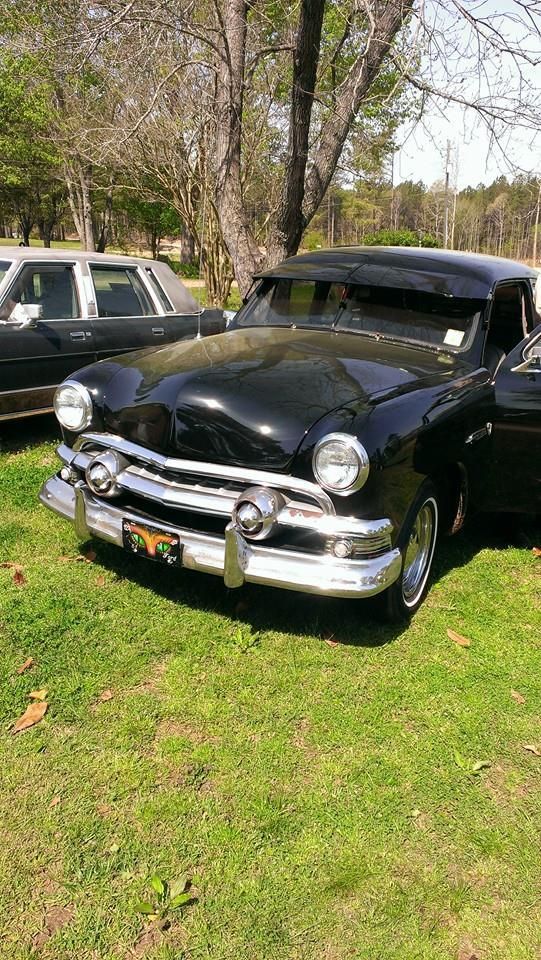 Black vintage Ford coupe parked on grass.