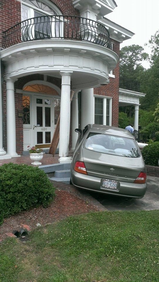 Car crashed into the porch of a brick building with white columns.