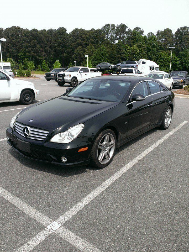 Black Mercedes-Benz sedan parked in an asphalt lot; other vehicles and trees in the background.