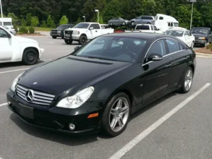 Black Mercedes-Benz sedan parked in an asphalt lot. Other vehicles and trees are visible in the background.