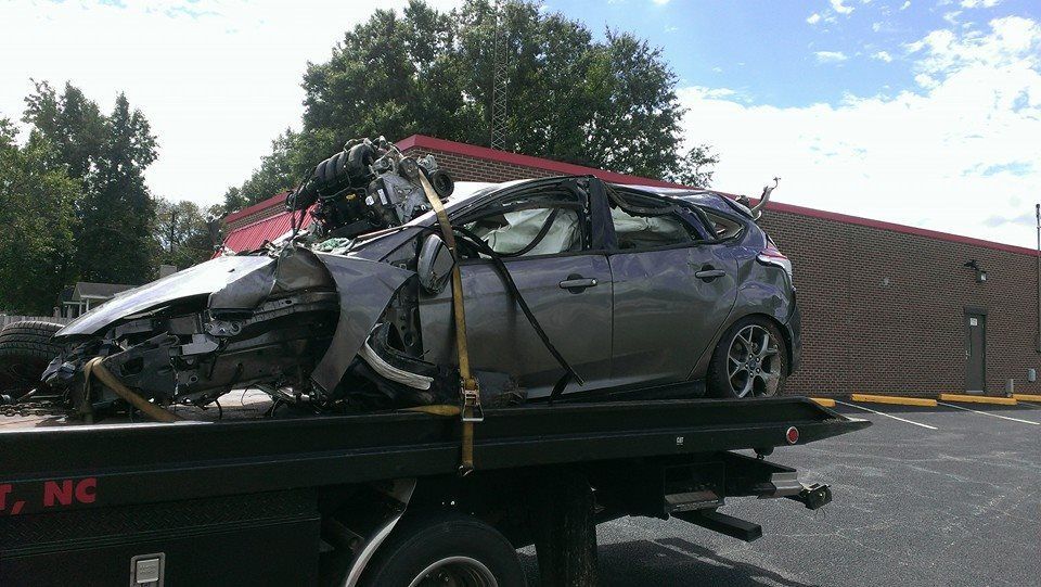 Severely damaged gray car on a tow truck, wrecked after an accident.