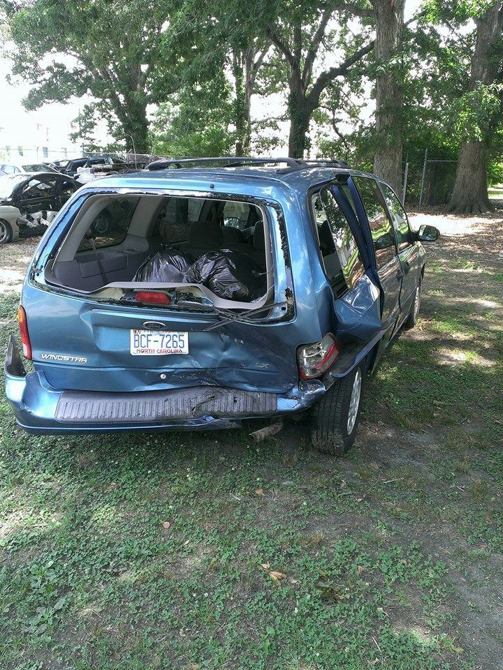 Damaged blue minivan after a collision, with a broken rear window and dented body.
