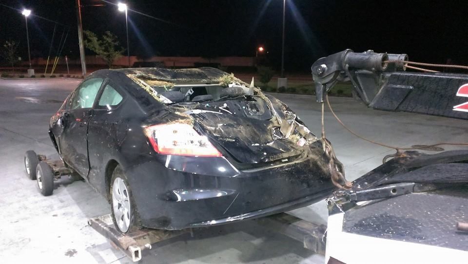 Black car severely damaged, being towed at night.