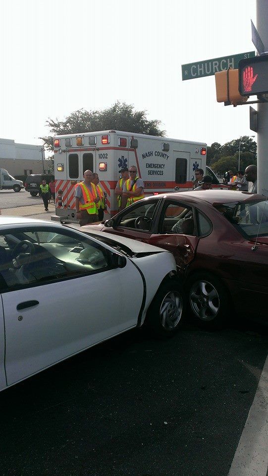 Two cars damaged in accident; ambulance and emergency personnel at intersection.