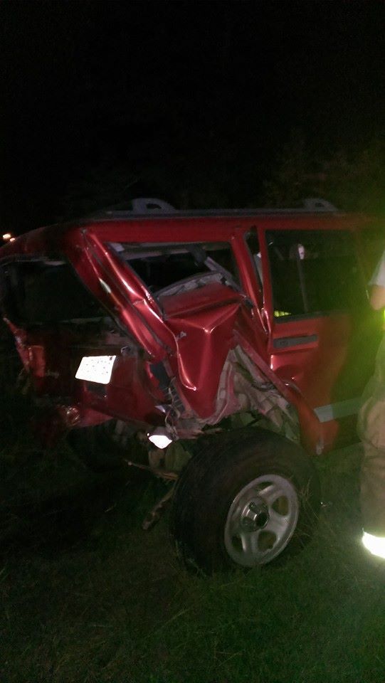 Red SUV with significant rear-end damage, likely from a collision, at night.