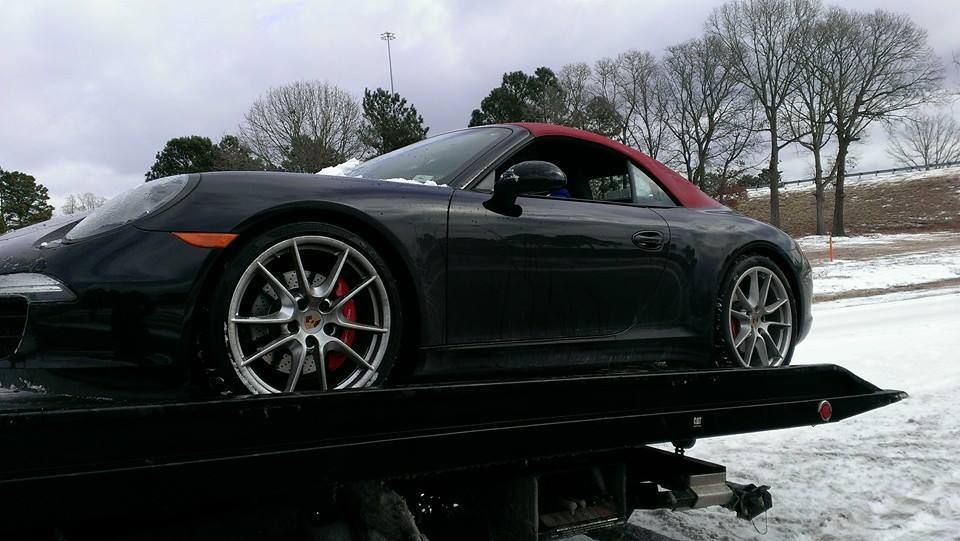 Black Porsche convertible on a tow truck in a snowy environment. Red convertible top and red brake calipers.