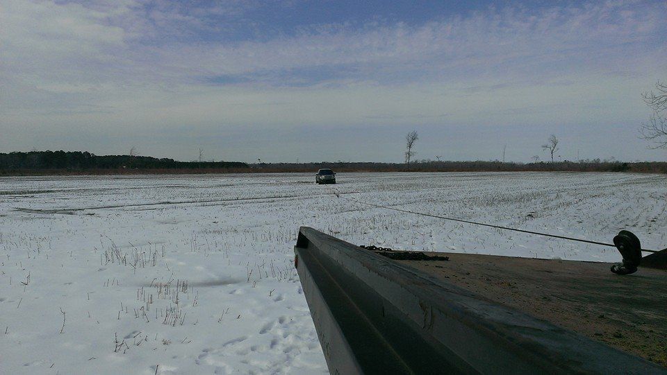 A vehicle being pulled across a snowy field by a rope; overcast day.