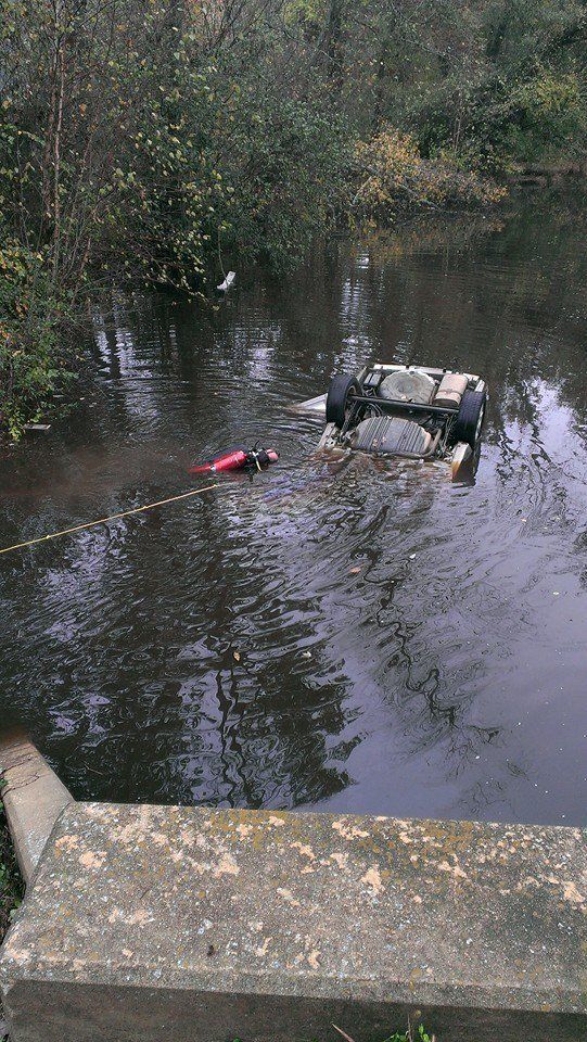 An overturned vehicle submerged in a river being pulled out by a rescuer.