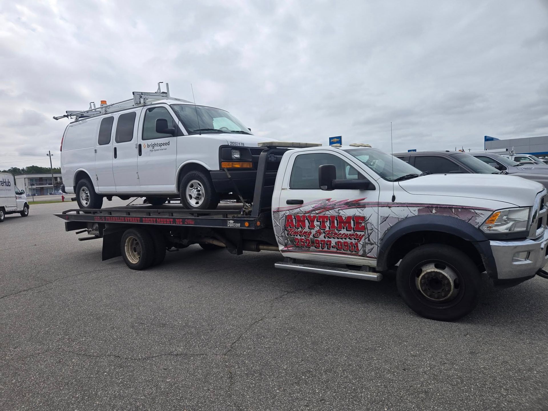White van being towed on a flatbed tow truck with the name 