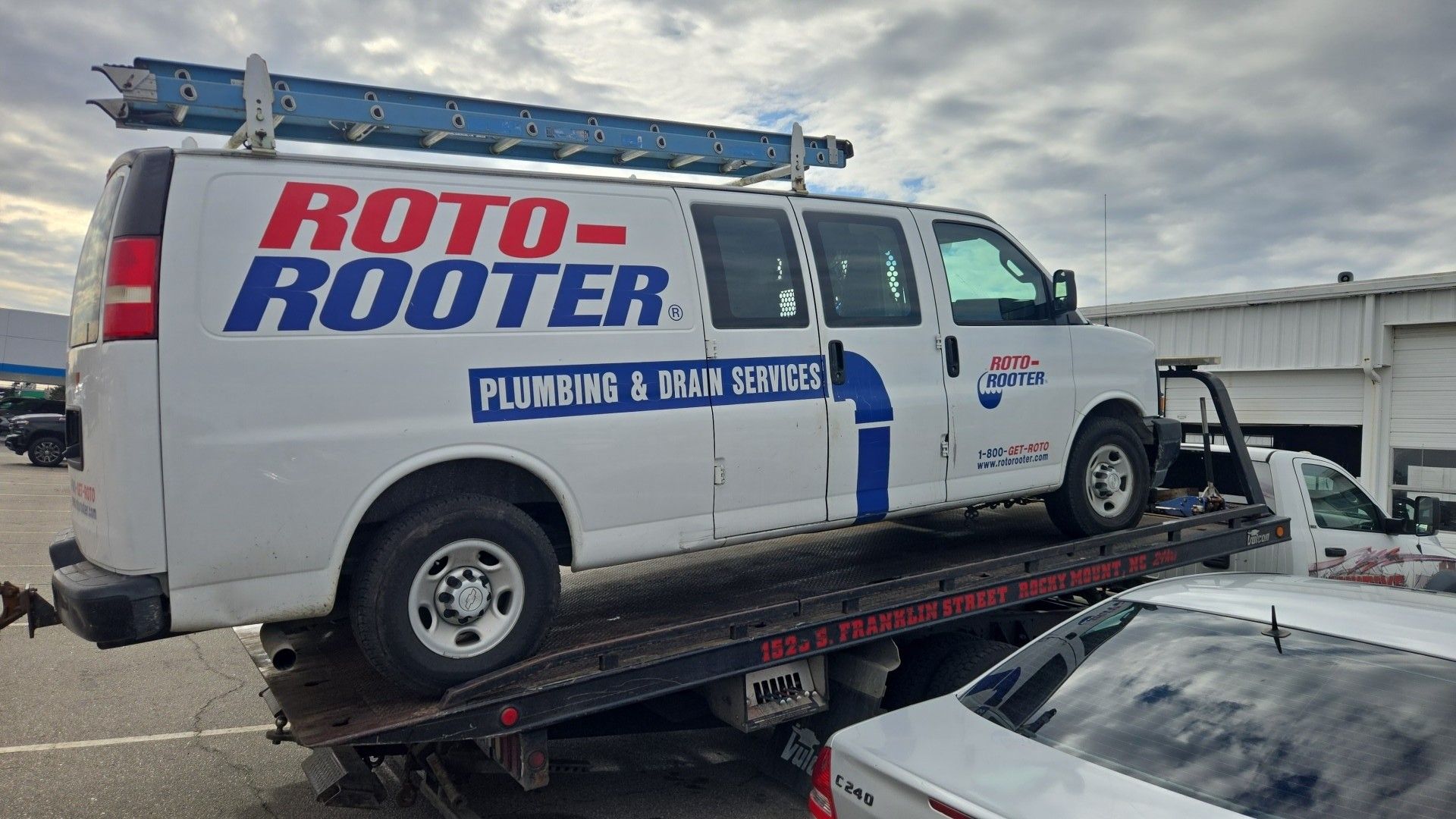 White Roto-Rooter plumbing van on a tow truck, ladder on top.