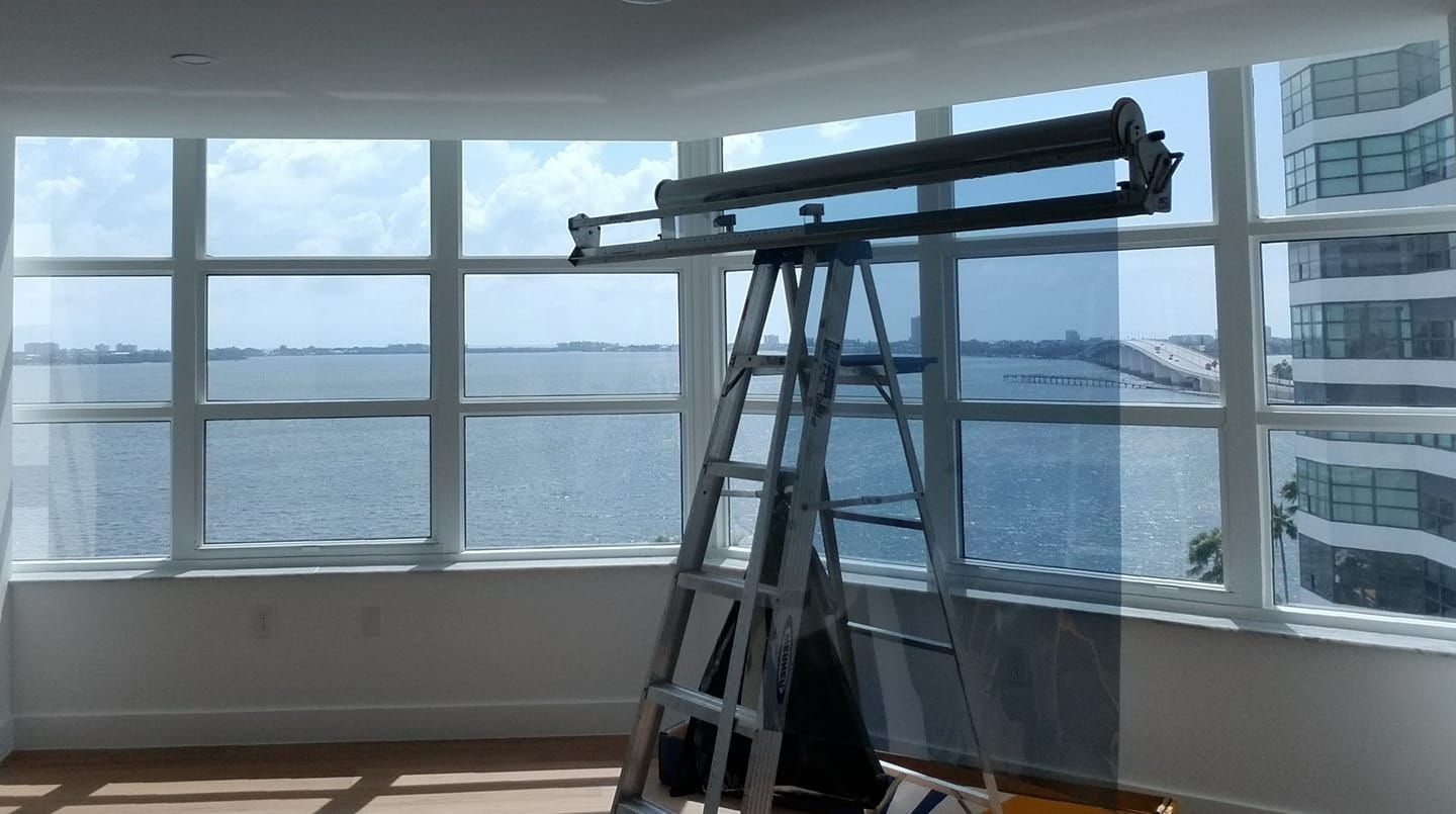 Ladder and roller shade being installed in a room with a waterfront view through large windows.