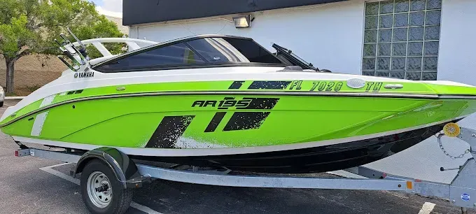 Bright green and white boat on a trailer, parked outside a building.
