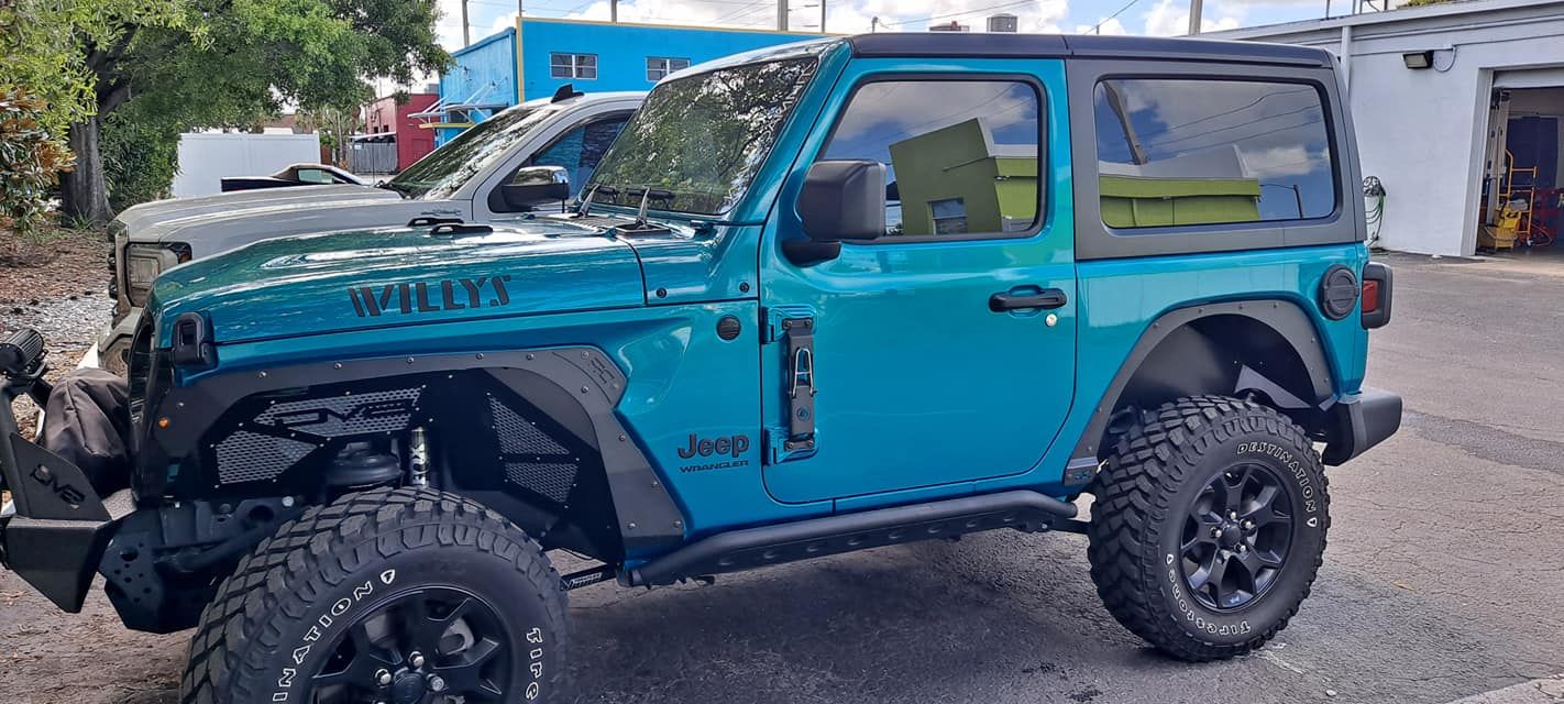 Teal Jeep Wrangler, black wheels, parked on a sunny day.