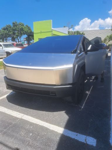 Tesla Cybertruck parked outdoors, person exiting the vehicle on a sunny day.