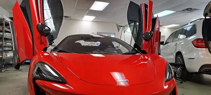 A red McLaren with its doors open inside a garage next to a white SUV.