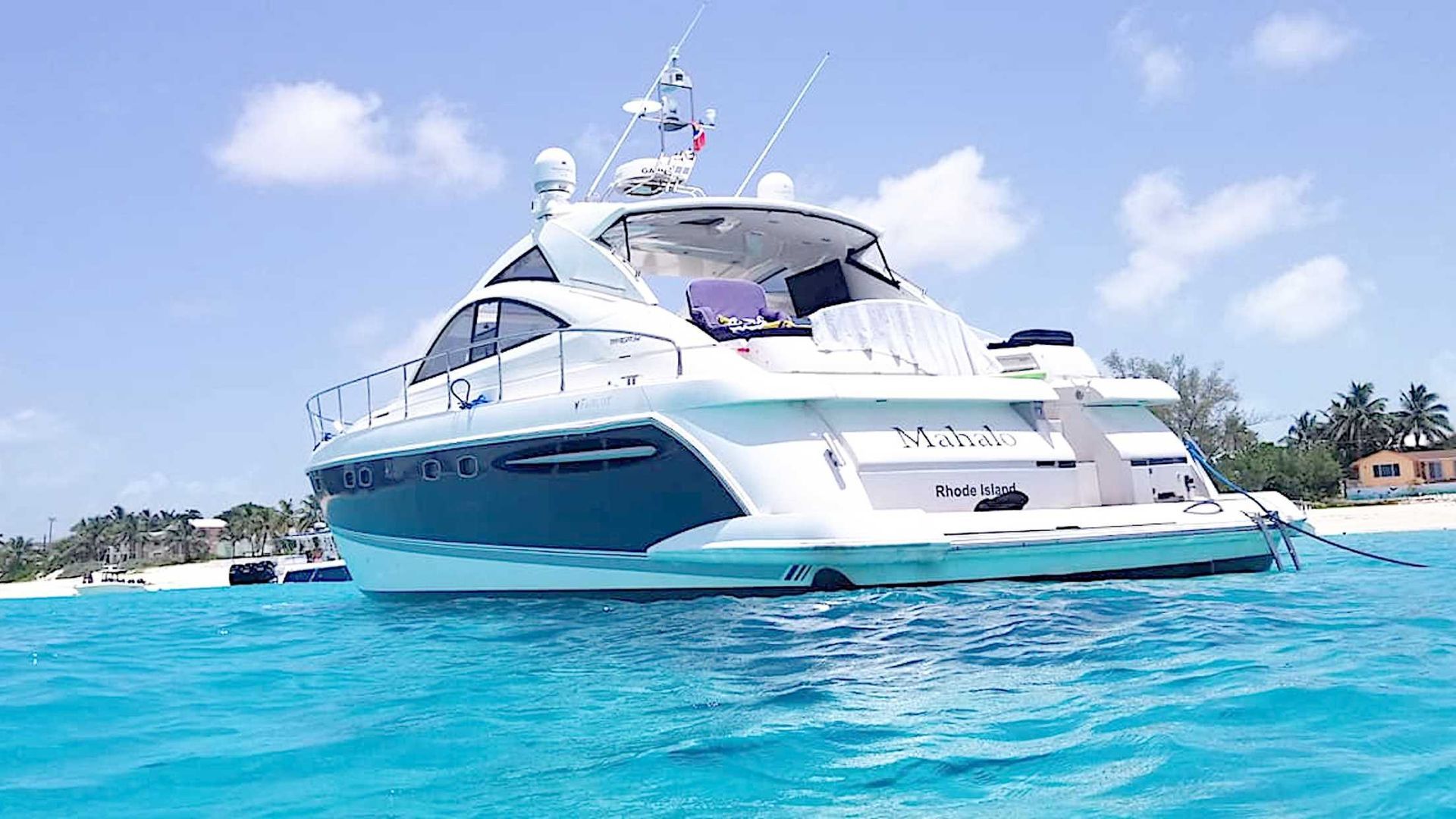 White and blue yacht in turquoise water near a sandy beach on a sunny day.