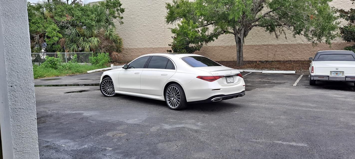 White Mercedes sedan parked in a lot with a light-colored building and trees in the background.