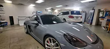 A gray Porsche in a garage with a white SUV.