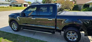 Black Ford F-150 pickup truck parked on a paved surface, in front of a house, in the suburbs.