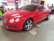 Red Bentley coupe parked in a garage with chrome accents and shiny wheels.