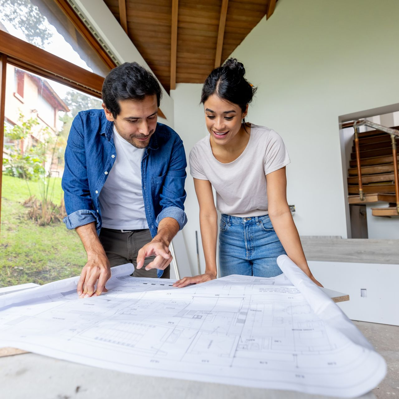 Two people reviewing blueprints in a bright room with exposed wooden ceiling.