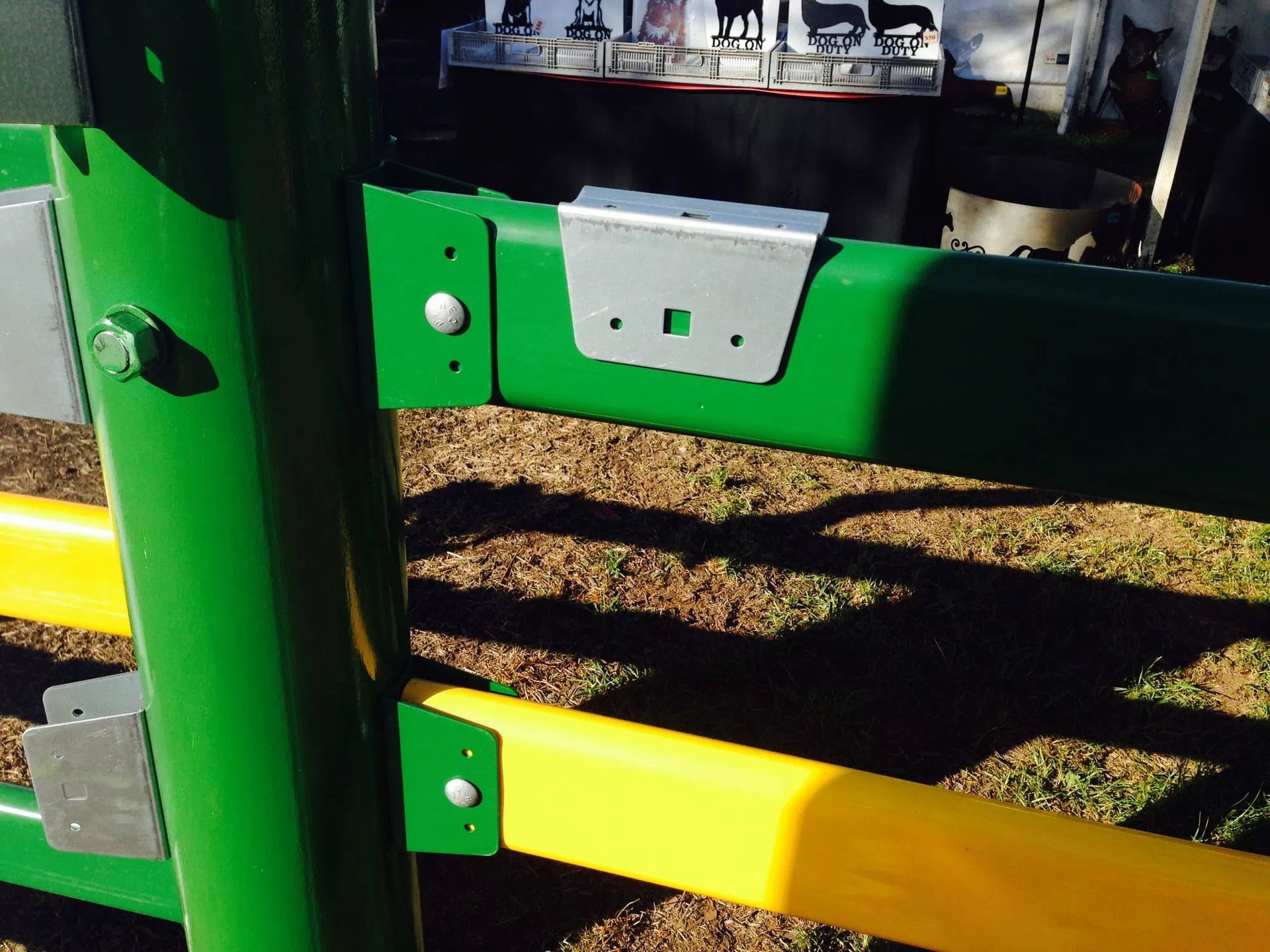 Close-up of a green fence post with two horizontal rails, one green and one yellow, attached by metal brackets.