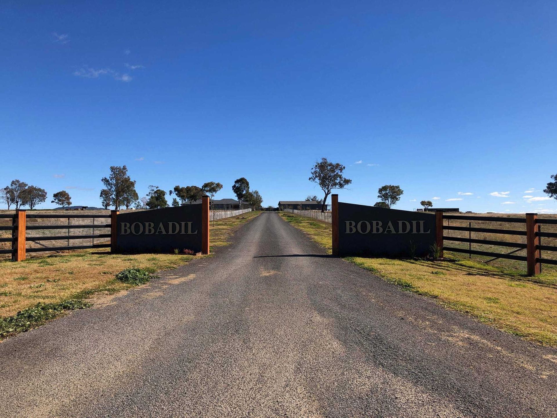 A gravel driveway leads through a gated entrance featuring dark signs that read