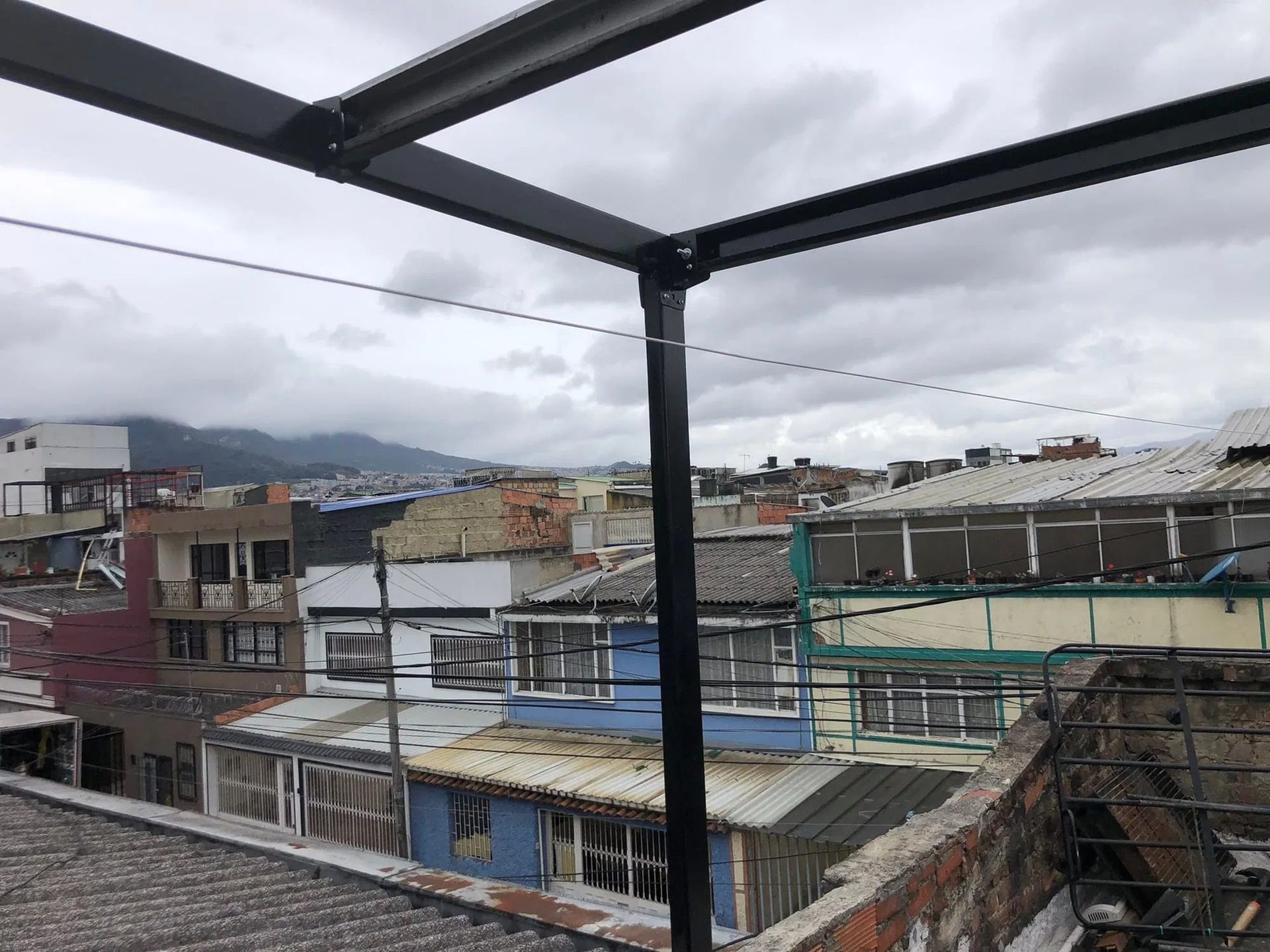 A view from a rooftop looking out over a dense urban neighborhood under a cloudy sky, framed by a metal support beam.