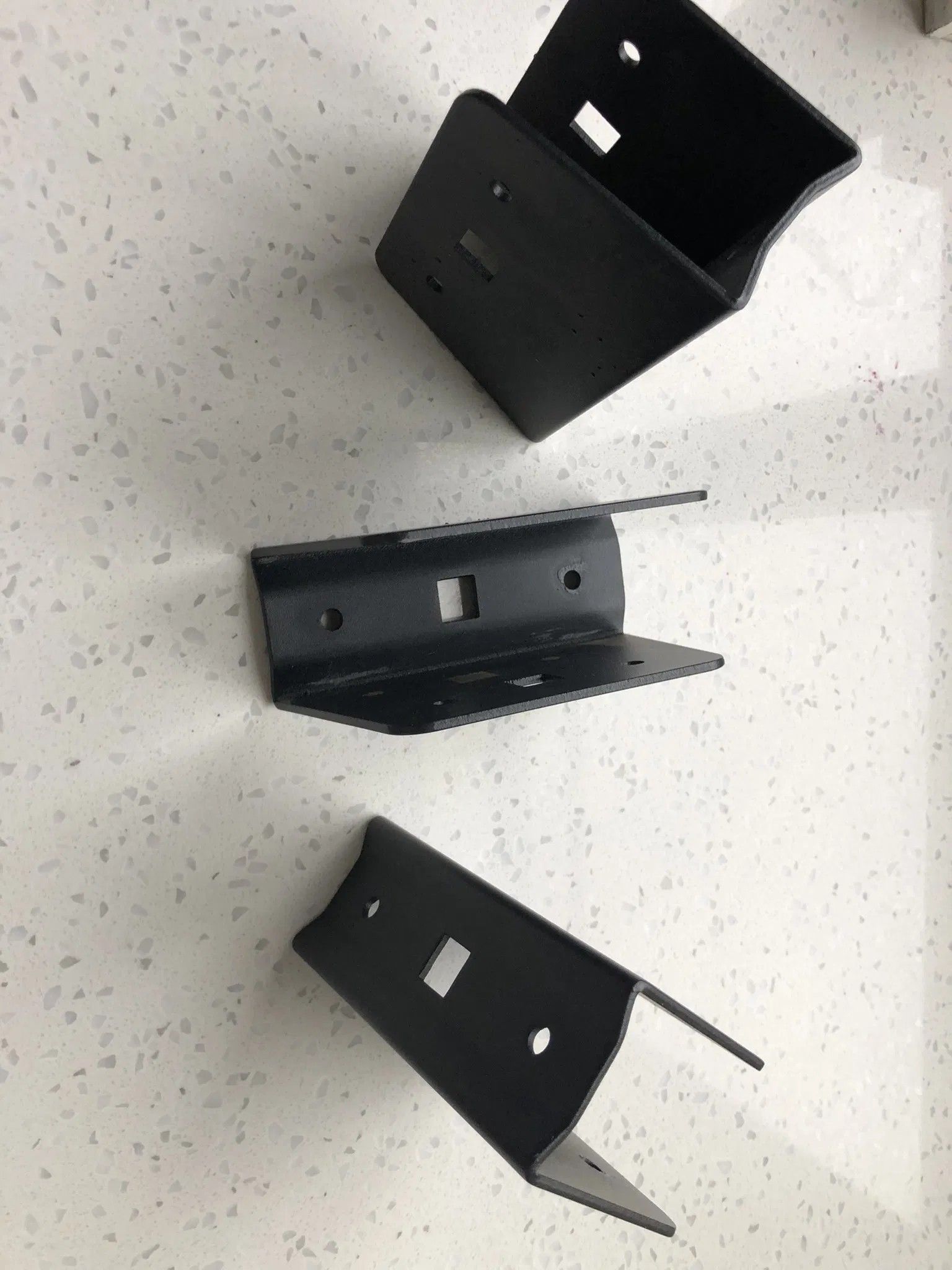 Three black metal, U-shaped fence rail brackets arranged on a white, speckled countertop.
