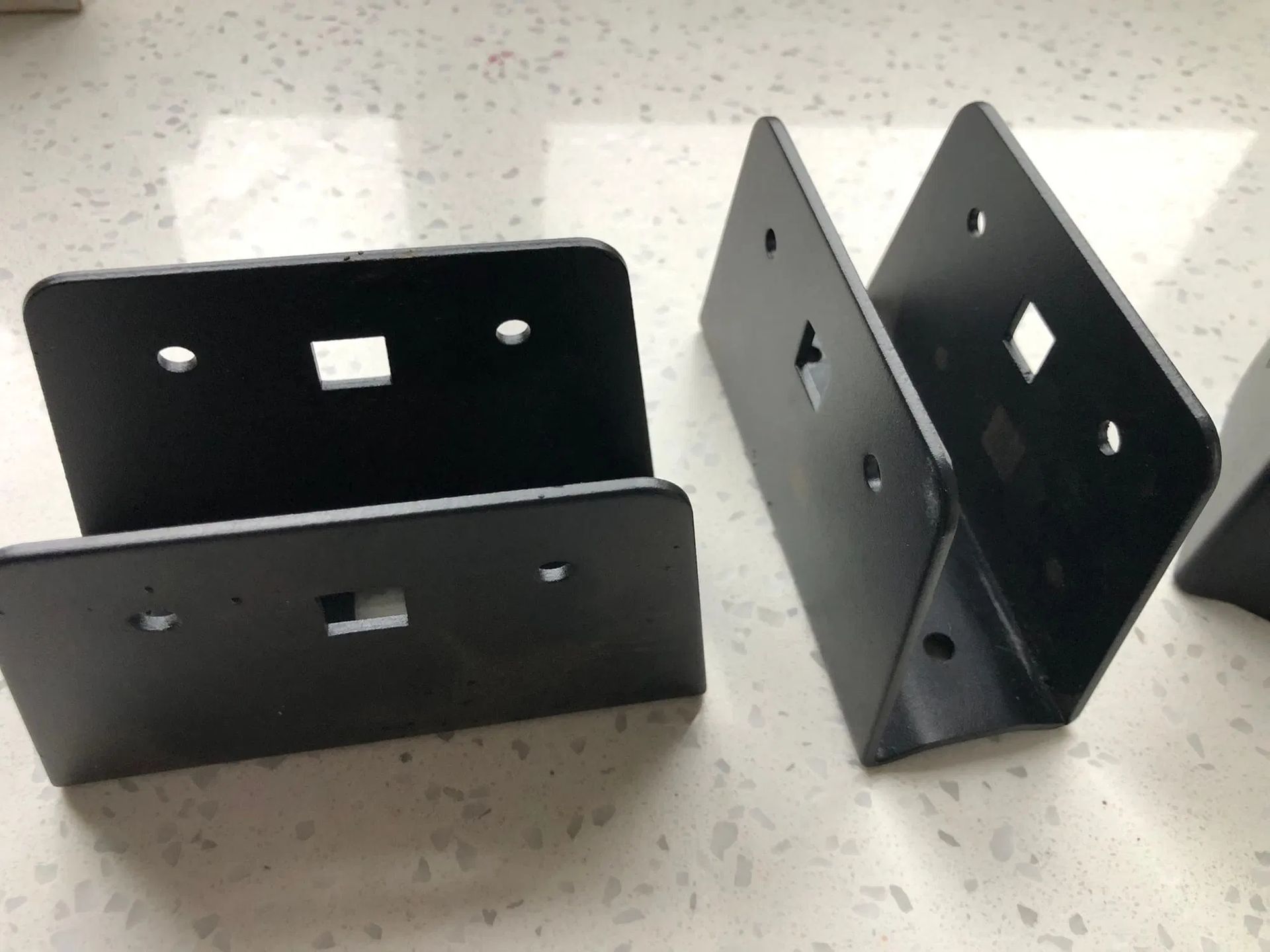 Two U-shaped black metal fence rail brackets with bolt holes sit on a white countertop.