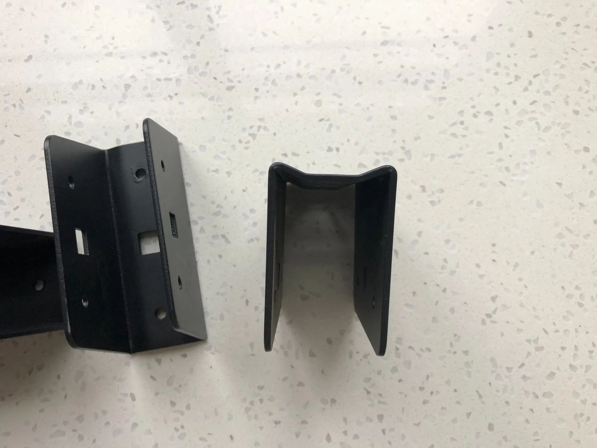 Two black metal U-shaped fence bracket components lie on a white surface.