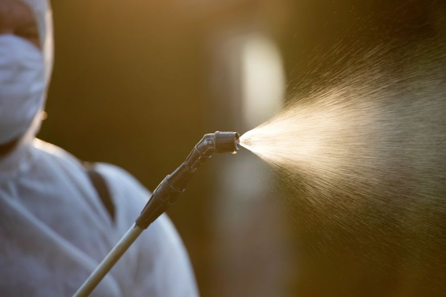 A man wearing a mask is spraying something with a sprayer.