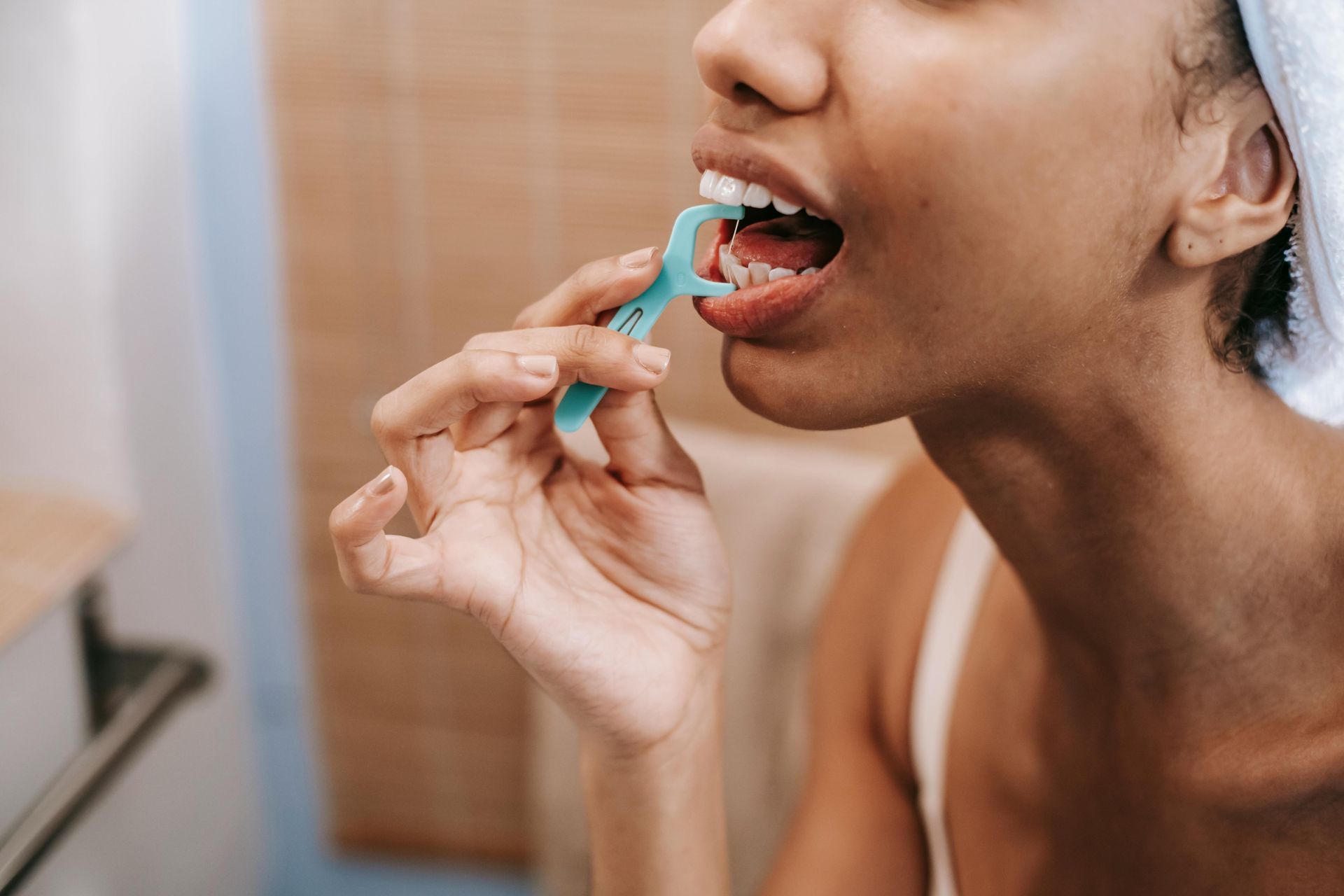 A woman flossing teeth with a blue floss pick in a bathroom.