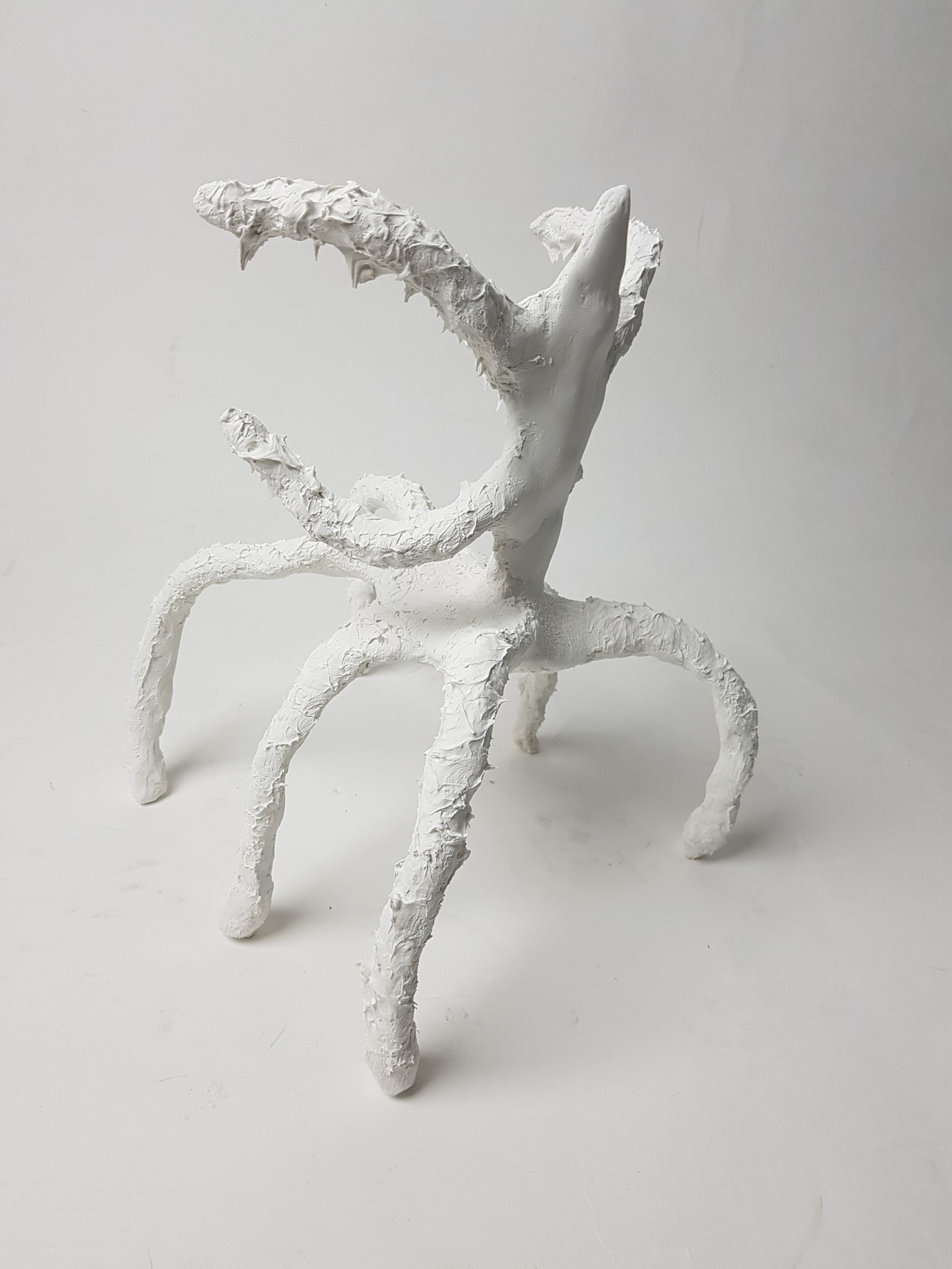 White abstract sculpture resembling a creature with spiky jaws, multiple legs, and textured surface.