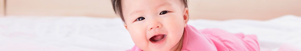 A baby in a pink shirt is laying on a bed.
