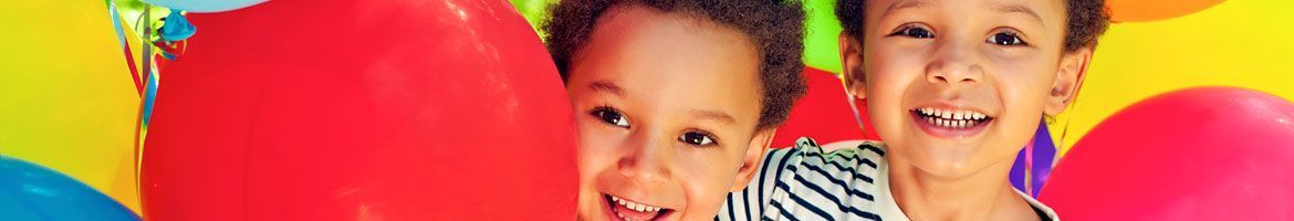 Three young boys are standing next to each other in front of balloons.