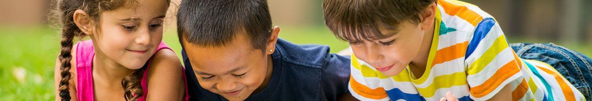 A group of children are laying on the grass looking at a tablet.